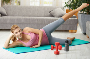 Young woman doing exercises lying on fitness mat in living room, smiling.